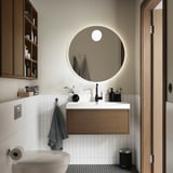 Salle de bains moderne avec lavabo en chêne brun ÄNGSJÖN, miroir rond, carrelage blanc, serviettes grises et accents noirs.