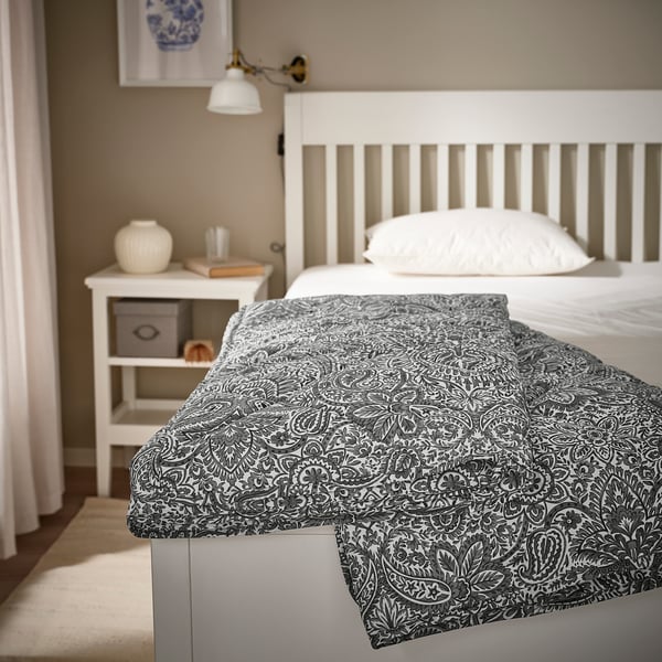 Couette ÄNGSSTAMFLY grise et blanche sur le lit, motif de feuilles, s’adapte bien.