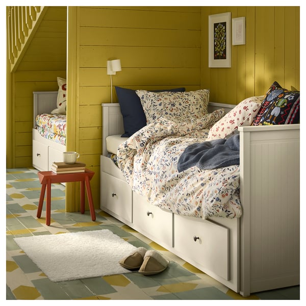 Une chambre douillette avec un lit blanc, des draps fleuris, des murs jaunes et un tapis blanc hirsute.