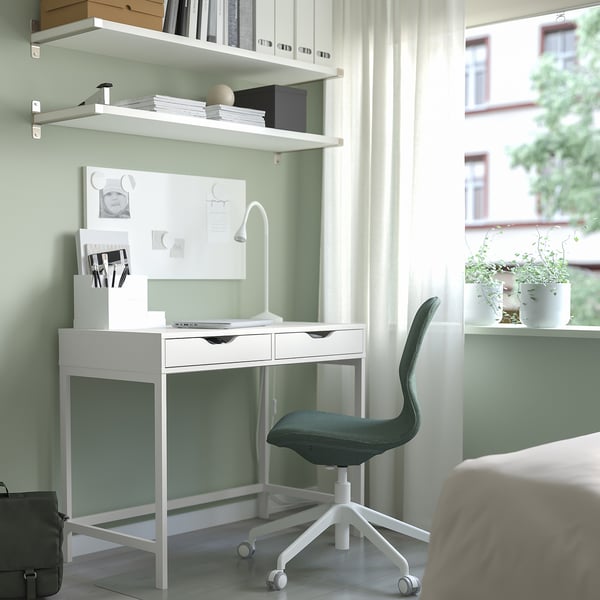 Petit bureau blanc avec deux tiroirs, une lampe et une chaise dans une pièce confortable.