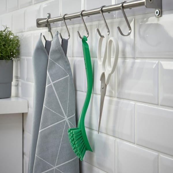 Un support de cuisine avec des ustensiles de suspension, y compris des serviettes grises, une brosse à vaisselle verte et des ciseaux blancs.