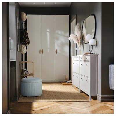 Entrée moderne avec armoire beige, pouf de rangement bleu, armoire à chaussures blanche, fleurs séchées et miroir rond.