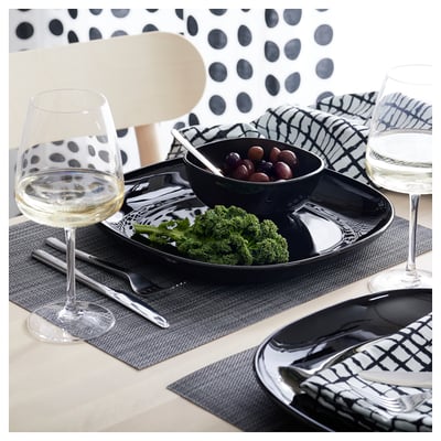Table moderne avec de la vaisselle carrée en verre noir, avec du brocoli et des raisins, accompagnés de verres à vin transparents.