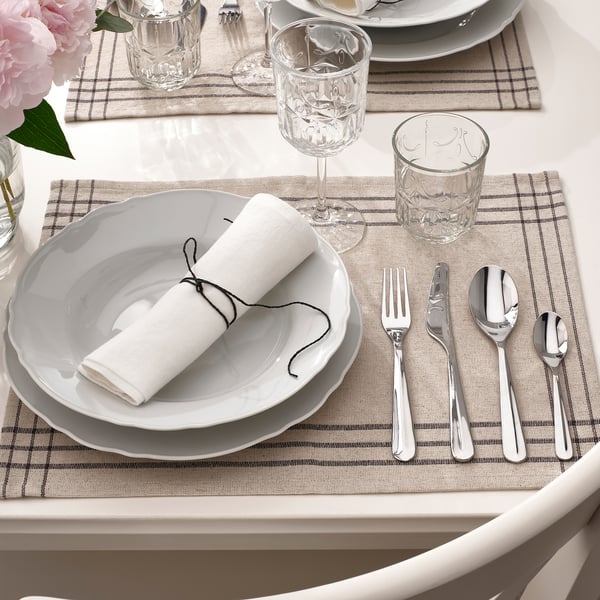 Table avec napperon gris, vaisselle blanche, serviette roulée, verrerie et couverts polis, y compris une fourchette, un couteau et une cuillère.
