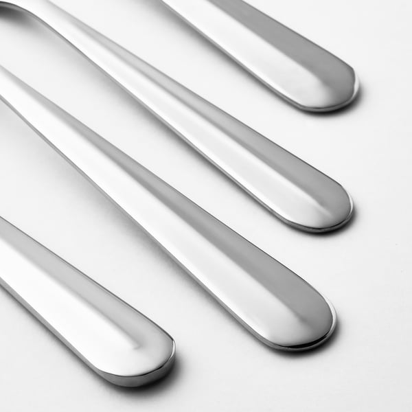 Quatre cuillères en acier inoxydable poli soigneusement alignées, poignées vers le bas, réfléchissant la lumière.