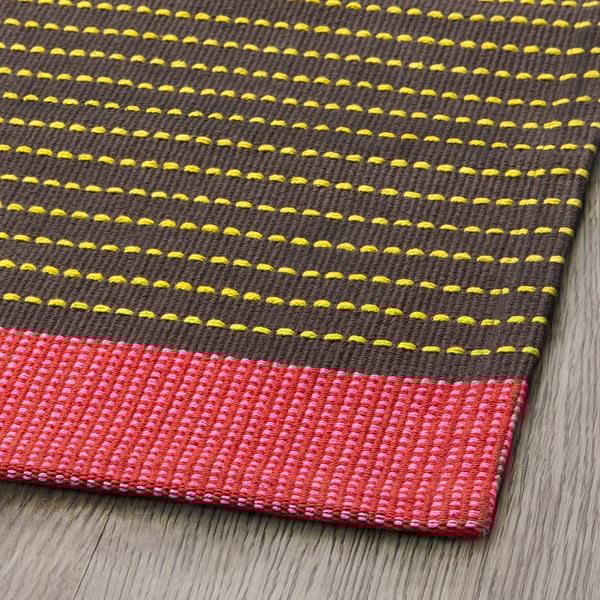 Tapis rayé coloré avec motif jaune et marron, bordure rouge sur surface en bois.