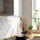 Cuisine moderne avec hotte en acier inoxydable, bord en verre, comptoir en bois, plantes et poêle à pâtisserie.