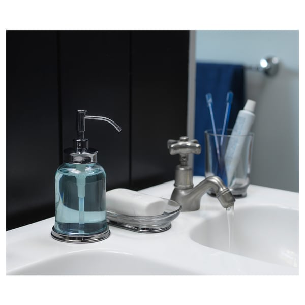 Distributeur de savon en verre et chrome sur évier blanc, teinté de bleu avec un style vintage.