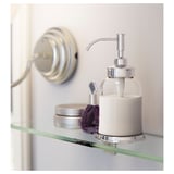 Un distributeur de savon BALUNGEN blanc sur une étagère en verre. Il a une pompe chromée et est entouré d’autres petits objets.