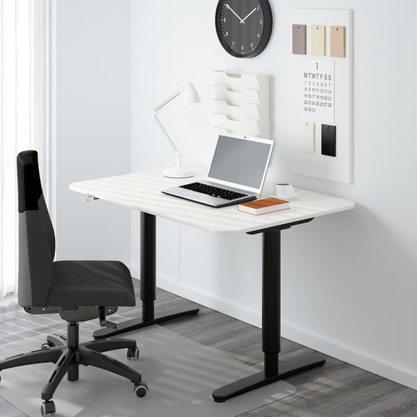 Bureau à domicile minimaliste avec bureau BEKANT blanc, chaise noire, ordinateur portable, lampe et organisateur mural.