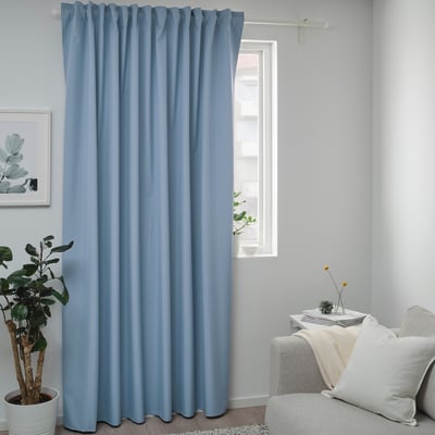 Les rideaux en polyester recyclé BENGTA pendent au-dessus d’une grande fenêtre, plus larges que l’usine, au sol. Canapé blanc avec oreillers à proximité.