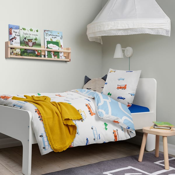 Coin chambre d’enfant avec literie sur le thème des véhicules, étagère, tabouret et lampe.