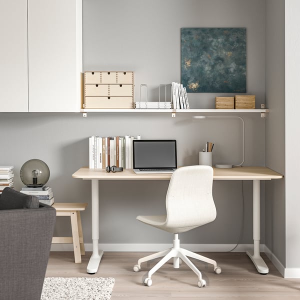 Configuration du bureau à domicile avec étagère murale BERGSHULT, chaise blanche, bureau en bois, œuvre d’art, livres et lampe. Design minimaliste.
