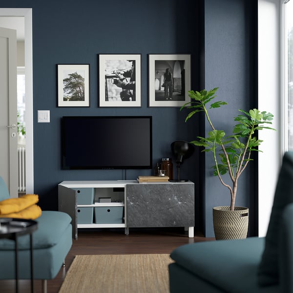 Salon moderne avec meuble TV, étagères et portes BESTÅ. Tv, photos, sièges bleus, plante.