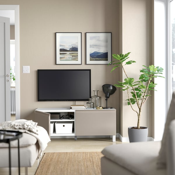Salon moderne avec meuble TV BESTÅ beige, télévision à écran plat, plante d’intérieur et photos de montagne encadrées.