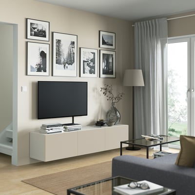 Salon moderne avec banc TV blanc BESTÅ, télévision noire, décor stylisé, photos encadrées en noir et blanc et grande fenêtre avec rideaux gris.