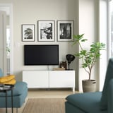 Salon moderne avec meuble TV BESTÅ blanc, télévision à écran plat, chaises turquoise et grande plante. Décoration d’œuvres d’art sur mur, atmosphère chaleureuse.