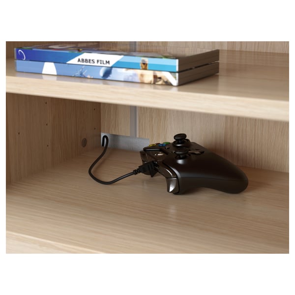 Une manette de jeu noire repose sur une étagère en bois à côté, un câble passe par un trou.