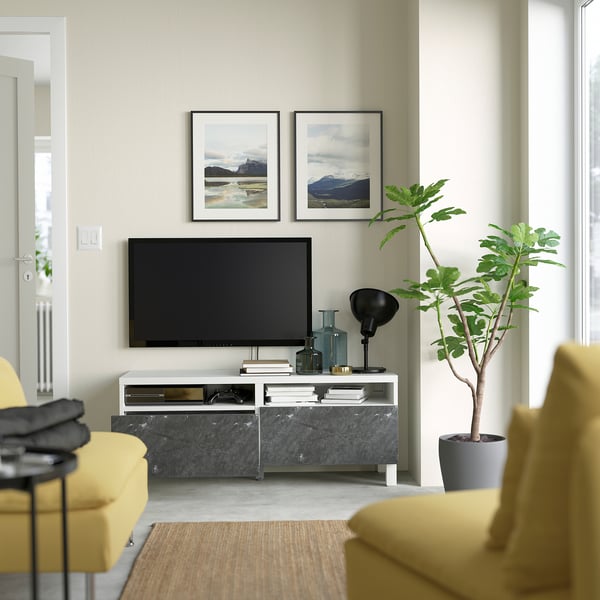 Salon moderne avec banc TV BESTÅ, télévision à écran plat, vases, plantes, chaises jaunes.