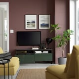 Salon moderne avec des murs marron, un meuble TV BESTÅ, des accents verts, une télévision à écran plat, des fauteuils jaunes et une grande plante.