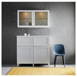 Coin repas moderne avec unité de rangement BESTÅ blanche, portes vitrées, chaise bleue, tapis jaune, mur gris foncé.
