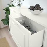 Armoire BESTÅ blanche avec tiroir ouvert révélant un panier en fil de fer. Décoré de plante, bol de sphères et d’algues dans un vase en verre.