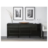 Buffet moderne en verre noir avec tiroirs et étagères. Surmonté d’un bol décoratif et de vases, contre un mur blanc avec des photos encadrées.