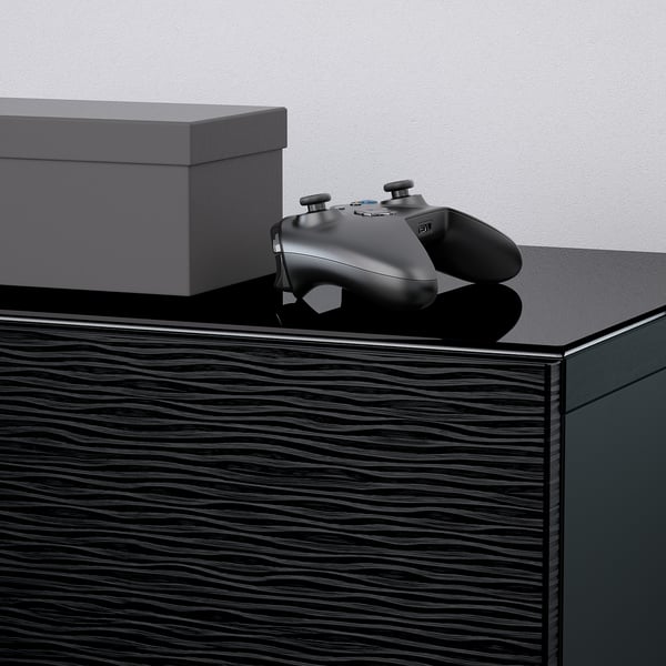 La manette de jeu noire repose sur une surface en bois sombre et brillante, à côté d’une boîte de rangement élégante et fermée.