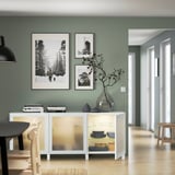 Salle à manger moderne avec buffet BESTÅ, portes vitrées montrant des assiettes, un vase et des photos.