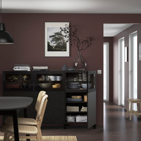 Salle à manger moderne avec buffet sombre, vaisselle, vase et chaises en osier.