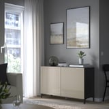 Salon moderne avec unité BESTÅ, art, plante, livres, bol, chaise noire, fauteuil près de la fenêtre.