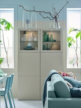 Salon moderne avec unité de rangement BESTÅ, vases, murs bleu clair et canapé.