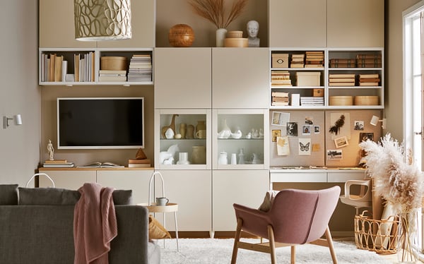 Espace de vie soigné avec des étagères BESTÅ de couleur claire, exposant des livres, des vases et des objets de décoration. Télévision à écran plat, chaises confortables et fleurs séchées.