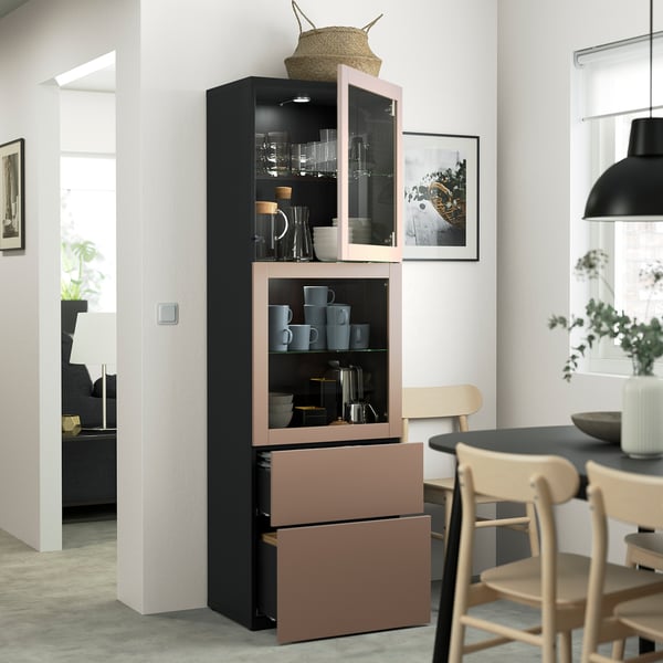 Une salle à manger moderne, une grande armoire BESTÅ avec des portes vitrées, des tasses et des bols, et des tiroirs en dessous pour un rangement caché.