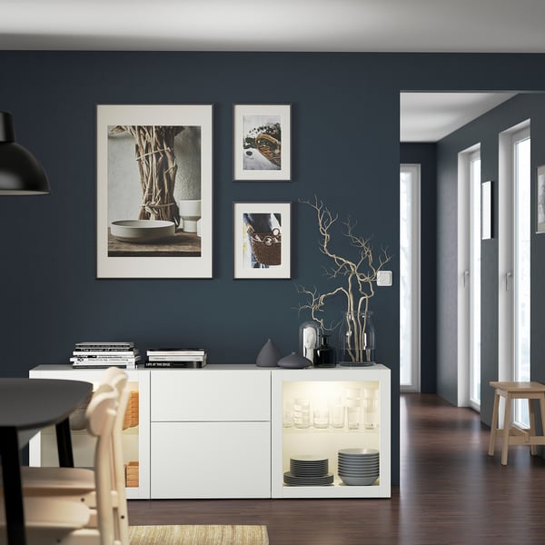 Salle à manger moderne avec buffet BESTÅ, verrerie, assiettes. Art minimaliste, parquet sombre, meubles clairs.