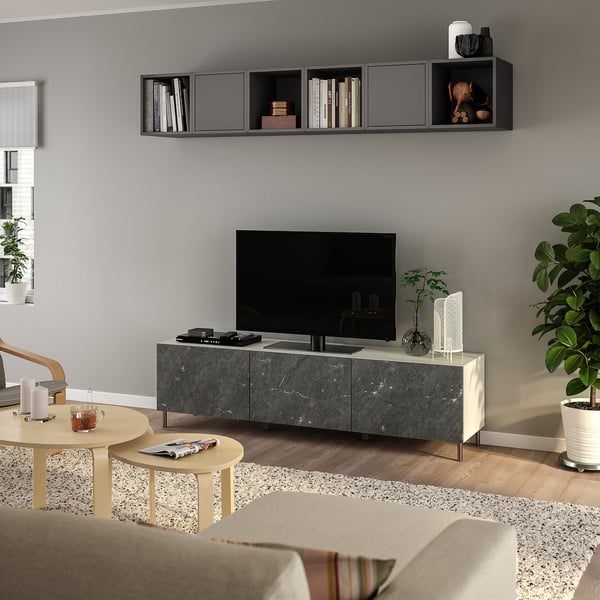 Salon moderne : meuble tv gris, étagères noires, canapé beige, tables en bois avec boissons, grande plante.