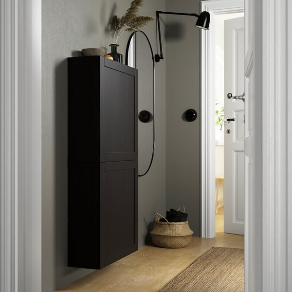 Armoire noire sur mur gris, 2 portes, étagère supérieure avec décor, panier en osier avec des articles.