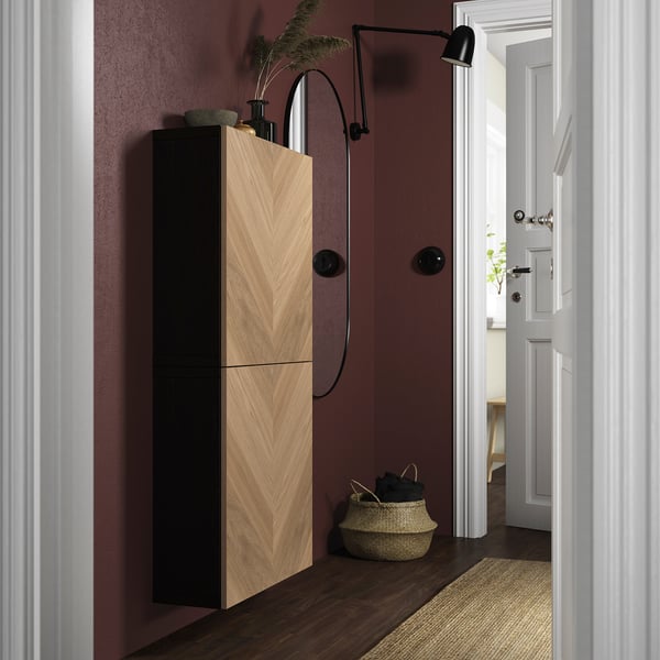 Couloir moderne avec murs marron, grande armoire en bois clair et noir, panier et applique murale. Porte ouverte sur une pièce lumineuse.