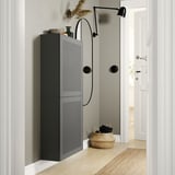 Couloir moderne avec armoire murale noire BESTÅ. Deux portes, un panier tressé en dessous, et une applique murale noire orientable.