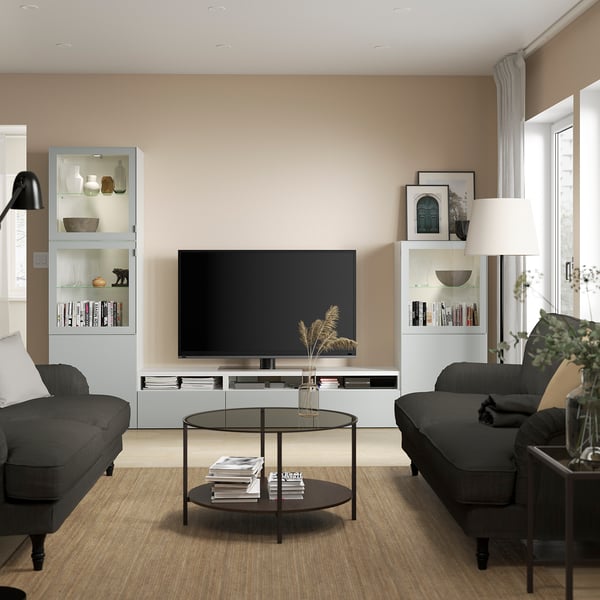 Salon moderne avec meuble tv BESTÅ, canapés noirs, décoration, livres, télévision, table basse et lampe.