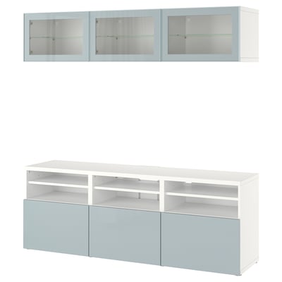 Unité de rangement BESTÅ blanche avec des accents bleus. Le dessus a des portes en verre, le bas a des étagères et des tiroirs ouverts. Design moderne et minimaliste.