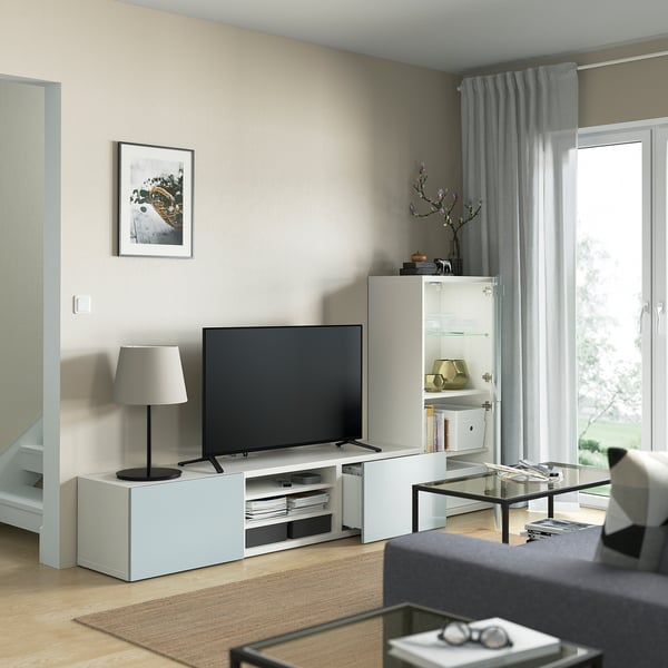 Salon moderne avec meuble TV BESTÅ, télévision à écran plat, table basse en verre, tapis gris, grande fenêtre avec rideaux et gestion soignée des câbles.
