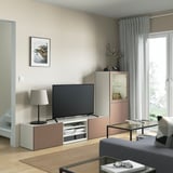 Salon moderne avec rangement TV BESTÅ, écran plat, étagères, tiroirs, armoire en verre, lampe, vase, art et rideaux de fenêtre.