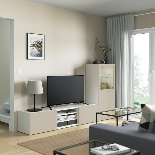 Salon moderne avec meuble TV BESTÅ, télévision à écran plat, lampe, armoire en verre et grande fenêtre avec rideaux gris.