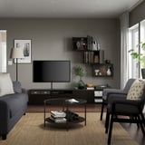 Salon moderne avec murs gris, canapé bleu, fauteuil gris, table basse, télévision, étagères, lampe et grande fenêtre.