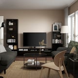 Salon moderne une unité de rangement TV BESTÅ avec étagères réglables, tiroirs et gestion des câbles. Une télévision noire et une chaise de revendeur reposent sur un tapis beige.
