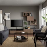 Salon contemporain avec canapé gris, télévision, table basse en verre, fauteuil à motifs, décoration murale et grandes fenêtres.