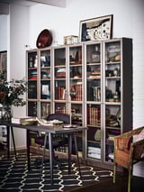 Étagère BILLY noire avec décoration et livres, à côté d’un bureau et d’une chaise en osier dans un bureau à domicile élégant.
