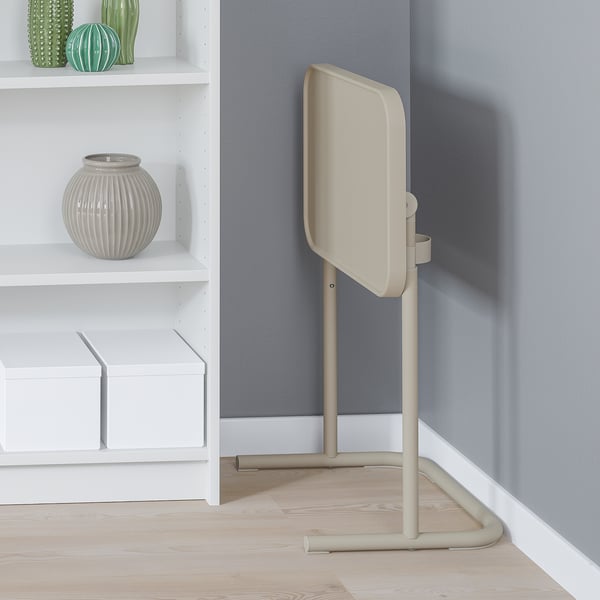 Support pour ordinateur portable beige à côté de l’étagère, incliné pour un travail confortable.