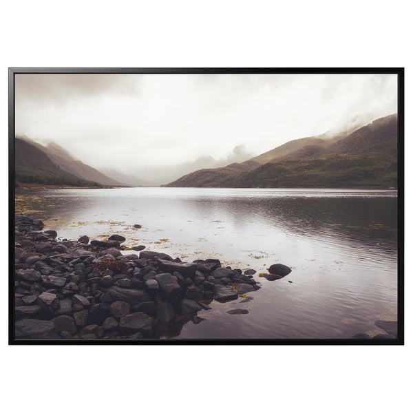 Cadre photo BJÖRKSTA : grand cadre rectangulaire en aluminium noir avec un imprimé de paysage montagneux à l’intérieur, avec un rivage rocheux et une eau calme.